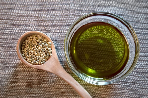 Wooden spoon with hemp seeds next to bowl of hemp seed oil